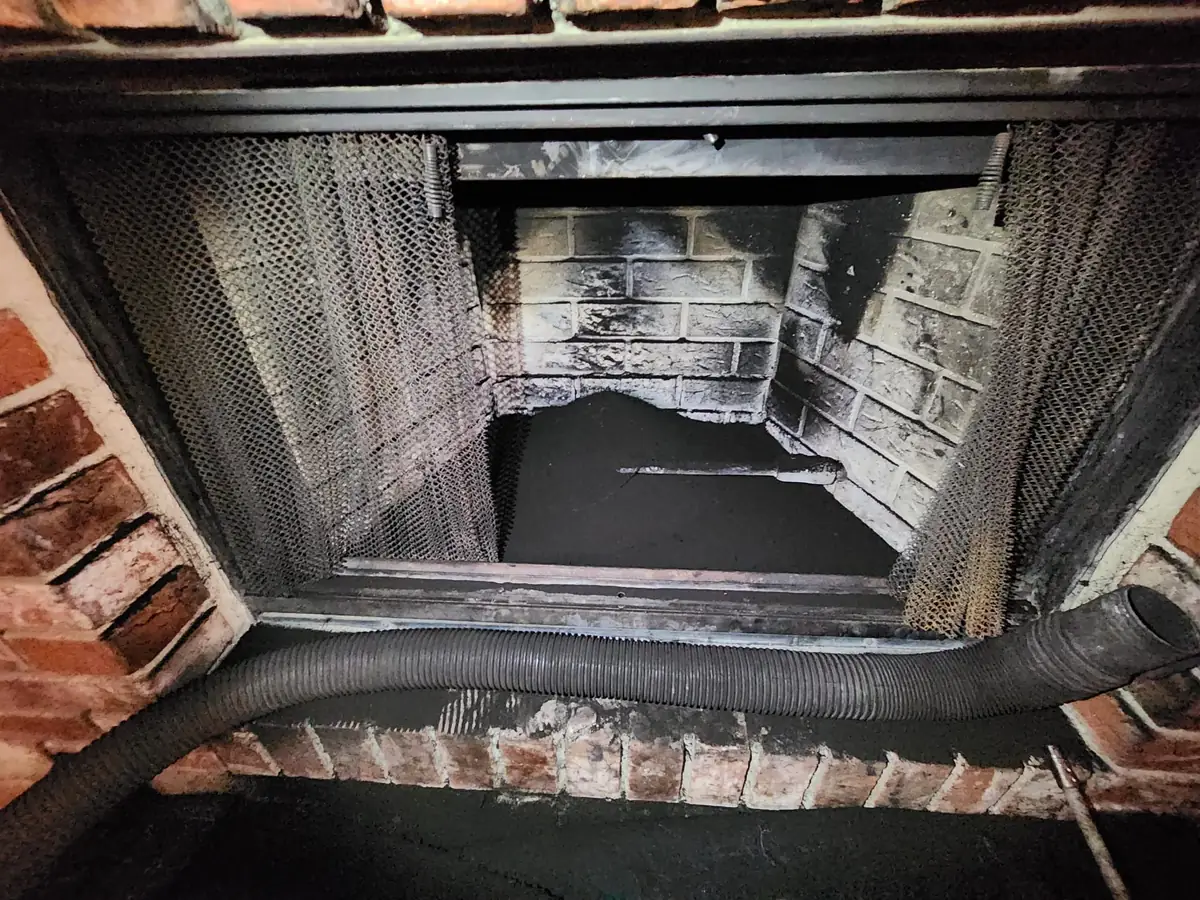 Soot-blackened firebox interior with the fire screen folded back and a sweep hose fed up past the damper