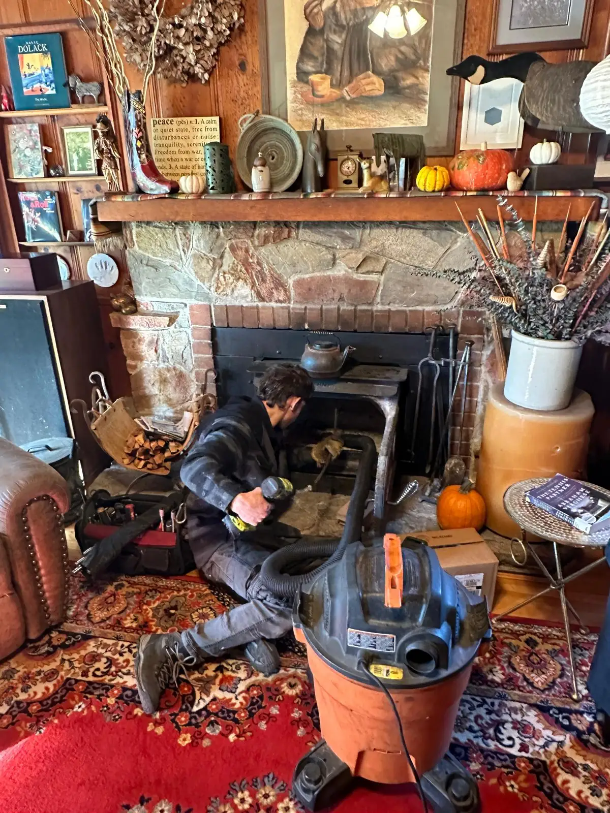 Fluora Prime technician kneeling at an open stone fireplace with a sealed HEPA vacuum running beside the hearth during a chimney sweep